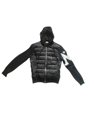 Moncler cardigan - Svart pufferjacka från Moncler med stickade ärmar och huva. Jackan har dragkedja framtill, quiltad front och en vit Moncler-logga på ena ärmen. Snygg kontrast med vit detalj på ärmen och dragsko i huvan. Perfekt för dig som vill ha en stilren och sportig look.