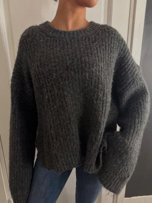 Mörkgrå oversized stickad tröja - Mysig mörkgrå stickad tröja med oversized passform och breda ärmar. Tröjan har grov ribbstickning och rund halsringning. Perfekt för lager på lager och en avslappnad look. Materialet känns mjukt och fluffigt.