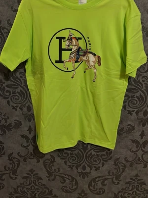 Grön t-shirt med hästtryck - Cool t-shirt i neon-grönt med stort tryck av en häst och ett H med texten Paris på bröstet. Perfekt statement-plagg för dig som vill sticka ut. Klassisk passform och rund halsringning.