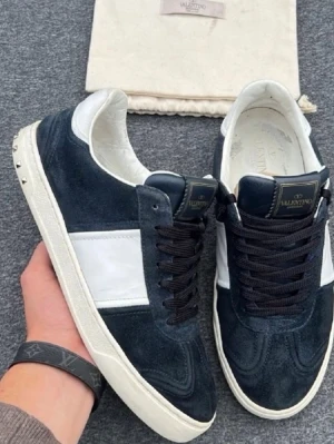 Valentino Garavani svarta sneakers - Snygga svarta sneakers från Valentino Garavani med vit sidopanel och svarta skosnören. Ovandelen är i mocka och detaljer i läder. Klassisk låg modell med vita sulor och små nitar på hälen för en extra touch. Perfekta för dig som gillar exklusiv streetstyle.skorna är oversize så typ 42 