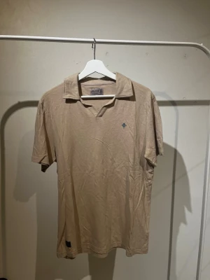 Beige pikétröja från Morris - Snygg beige pikétröja från Morris med klassisk krage och korta ärmar. Tröjan har en liten broderad detalj på bröstet och är tillverkad i mjuk bomull. Perfekt för en avslappnad men stilren look.