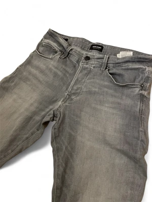 Jack and jones jeans - Snygga grå slim fit jeans från Jack & Jones med klassisk femficksdesign och diskret broderad bakficka. Storlek W32 L34 modell slim/glenn