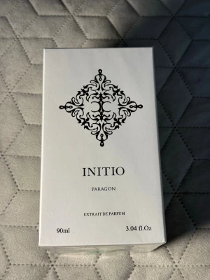 Initio Paragon Extrait de Parfum 90ml - Initio Paragon Extrait de Parfum är en exklusiv parfym i en elegant vit kartong med svart dekorativt mönster. Flaskan rymmer 90 ml och doften är känd för sin intensitet och lyxiga känsla. Perfekt för dig som vill sticka ut med en unik signaturdoft.