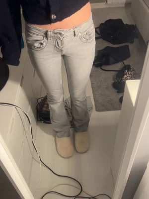 Ljusgrå bootcut jeans - Säljer ett par ljusgrå bootcut jeans med låg midja och klassiska fem fickor. Jeansen har en snygg tvätt och sitter tajt över låren för att sedan bli vidare nedtill. Perfekta för en trendig och avslappnad look.