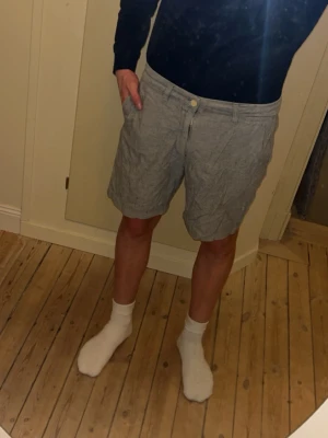 Gråa shorts i linne från H&M - Snygga grå shorts från H&M i linne med klassisk passform och midwaist. De har fickor på sidorna, bälteshällor och stängs med knapp och dragkedja. Perfekta för varma dagar och enkel att matcha med olika outfits.