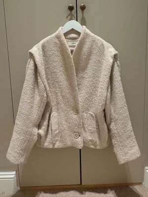 Isabel Marant Drogo jacket  - ”Drogo Jacket With Shoulder Detail by Isabel Marant Etoile is a stylish choice for those seeking a blend of elegance and comfort. This jacket is crafted with a unique wool blend, offering a luxurious feel and a chic silhouette. - Outer Material: 50% Wool, 18% Acrylic, 13% Polyamide, 12% Polyester, 7% Mohair - Sleeve Lining: 53% Viscose, 47% Cupro - Body Lining: 100% Cotton - Dry clean only” Nypris: 9000kr