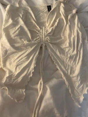 Vit croppad topp med snörning - Trendig vit croppad topp från hm med snygg snörning framtill och vågiga kanter. Toppen har korta ärmar och är perfekt för dig som gillar en modern och ungdomlig stil.