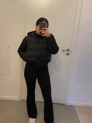 Svart pufferjacka med huva (petite) - Säljer en svart pufferjacka från Missguided (petite) med huva och dragkedja samt knappar framtill. Jackan är kortare i modellen. Klassisk och stilren design som passar till det mesta.