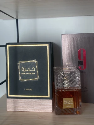 Khamrah parfym från Lattafa - Khamrah parfym från Lattafa med elegant glasflaska och detaljerad design. Flaskan är genomskinlig med guldlabel och innehåller en bärnstensfärgad vätska. Levereras i en lyxig svart och guld ask med trädetalj. Perfekt för dig som gillar exklusiva dofter.