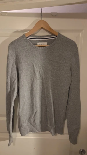 Grå tunnare sweatshirt Pier One - En stilren grå tröja från Pier One med rund halsringning och ribbade muddar vid ärmslut och nederkant. Perfekt för en enkel och clean look. Tillverkad i mjukt material som känns skönt mot huden. Aldrig använd men ingen prislapp.
