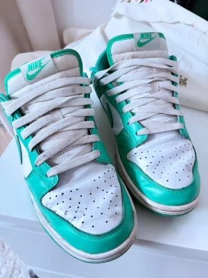 Nike Dunk Low clear jade - Säljer ett par Nike Dunk Low sneakers i vitt och grönt. Skorna har klassisk låg profil, gröna detaljer och vit bas med perforerad tå. Nike-logga på tungan och sidan. Perfekta för dig som gillar streetstyle och sportig look.