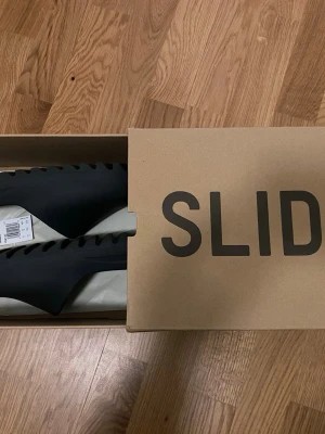 Svarta Yeezy Slide sandaler - Svarta Yeezy Slide sandaler från Adidas med stilren och chunky design. Tillverkade i mjukt och flexibelt syntetmaterial med bred rem över foten och räfflad sula för extra grepp. Perfekta för en avslappnad och trendig look. Behöver ni fler bilder så är det bara att skriva!