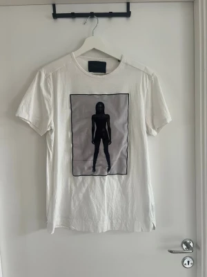 Vit t-shirt med konstmotiv från limitato - Vit t-shirt från limitato med ett stort konstnärligt tryck på framsidan som föreställer en siluett av en person. T-shirten har rund hals och korta ärmar. Materialet ser ut att vara mjukt och lätt, perfekt för en avslappnad look.