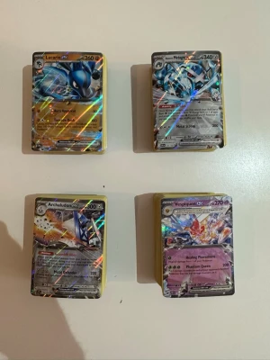 Ca 400 blandade pokemonkort  - Säljer fyra högar med Pokémonkort, där de översta korten är Lucario GX, Metagross GX, Archaludon GX och Vespiquen GX. Korten har holografisk effekt och färgstarka motiv. Perfekt för samlare eller Pokémonfans som vill utöka sin samling.