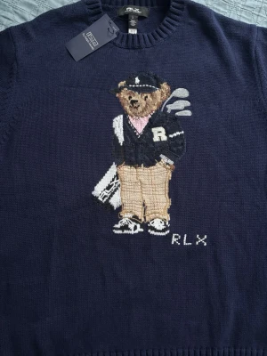 Ralph Lauren stickad tröja Polo Bear - Väldigt bekväm mörkblå stickad tröja från Polo Ralph Lauren med ikoniska Polo Bear-motivet framtill. Björnen har golfkläder och klubbor, och RLX-broderi finns nedtill. Perfekt nu i vintern och inför våren. Storlek L men passar M väldigt bra. Pris går att diskutera enbart vid snabbaffär.