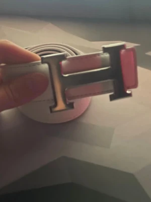 Vitt skärp med H-spänne - Säljer ett stilrent vitt skärp från Hermès med ett ikoniskt H-formad spänne i silver. Skärpet är tillverkat i skinn och har en klassisk design som passar perfekt till jeans eller kostymbyxor. Perfekt accessoar för att lyfta din outfit.