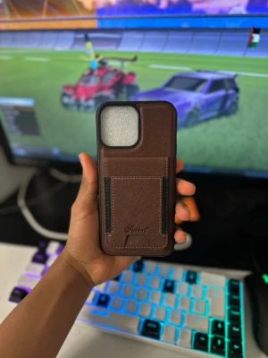 Brunt mobilskal med kortfack i läder - Snyggt brunt mobilskal från Shuter i konstläder med praktiskt kortfack på baksidan. Skalet har en stilren design och är anpassat för trådlös laddning. Perfekt för dig som vill ha både skydd och funktion i ett skal.