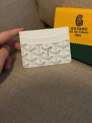Vit kortfodral från Goy4ard - Snyggt vitt kortfodral från Goy4ard med det klassiska mönstret och loggan framtill. Tillverkat i exklusivt läder med flera fack för kort. Perfekt för dig som vill ha en stilren och lyxig accessoar i fickan.
