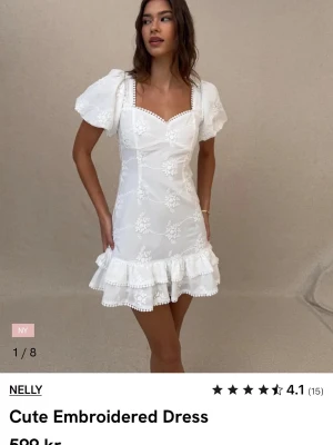 Vit broderad kortklänning från Nelly - Broderad vit klänning med puffärmar, v-ringad hals och volangkant nedtill. Klänningen har öppen rygg med knytband och blommigt mönster. Aldrig använd och prislapp kvar. Öppen för prisförslag
