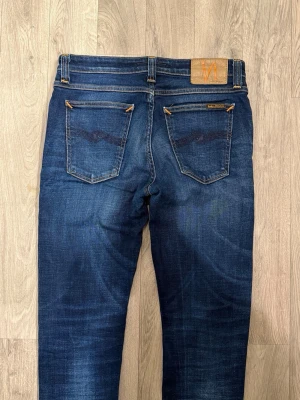 Nudie Jeans Mörkblå W30/L32 - Skinny/Slim Fit - Mycket fint skick. Mått - Midja: 37,5cm, Ytterbenslängd: 105cm, Benöppning: 14,5cm. Modellen är 185cm & 63kg. Hör av dig vid funderingar!🤝