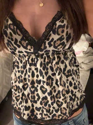 Leopardmönstrat linne med spets - Snyggt linne med leopardmönster. Det är en djup v-ringning med svarta spetsdetaljer, tunt axelband och luftig passform.