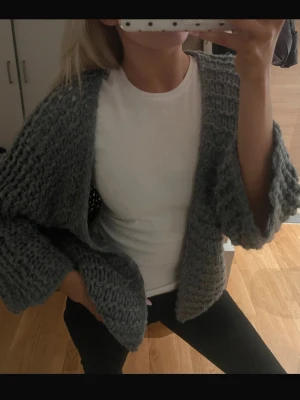 Grå chunky stickad kofta - Säljer en oversized, handstickad kofta i chunky grått garn. Koftan har breda ärmar och öppen front, perfekt att slänga på sig över en t-shirt. Supermjuk och mysig, passar dig som gillar en avslappnad och trendig stil.