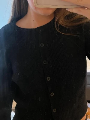 Svart stickad glittrig kofta från Bik Bok - Säljer en svart stickad kofta från Bik Bok med långa ärmar och knappar framtill. Koftan har en rak, lite croppad passform och ribbade muddar vid ärmslut och nederkant. Perfekt att slänga över en topp för en enkel och snygg look.