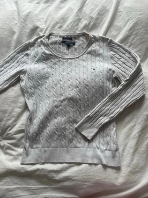 Vit kabelstickad tröja från Gant - Orginalpris 1360kr. Kabelstickad vit tröja från Gant med rund halsringning och diskret broderad logga på bröstet. Tröjan har långa ärmar och ribbade muddar vid ärmslut och nederkant. Klassisk och stilren design i mjukt material. 