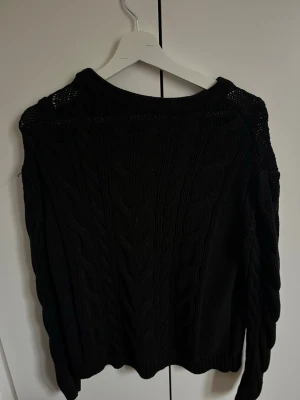 Svart kabelstickad tröja - Säljer en svart kabelstickad tröja med rund hals och långa ärmar. Tröjan har ett klassiskt flätmönster och är gjord i ett mjukt, tjockt material som passar perfekt för kyligare dagar. Enkel och stilren design som är lätt att matcha.
