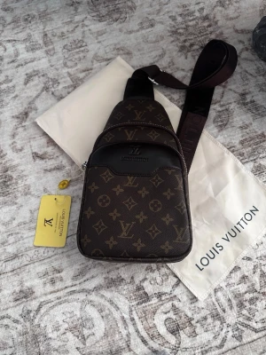 Louis Vuitton brun monogram rygg/axelväska - Snygg brun rygg/axelväska från Louis Vuitton med klassiskt monogrammönster och justerbar axelrem. Väskan har flera fack med dragkedja och är tillverkad i canvas med läderdetaljer. Perfekt för dig som vill ha en trendig och exklusiv accessoar.