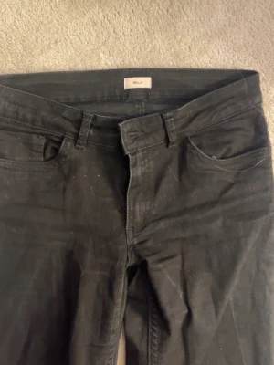 Svarta bootcut jeans med låg midja - Säljer ett par svarta bootcut jeans med låg midja och klassisk femficksdesign. Jeansen har utsvängda ben, perfekta för en avslappnad men trendig look. Materialet är stretchigt denim som sitter snyggt och bekvämt.