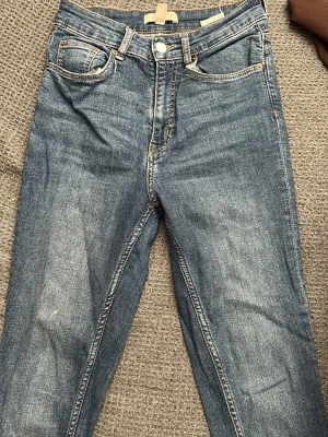 Blå smala jeans med fyra fickor - Säljer ett par klassiska blå jeans med smal passform och fyra fickor. Jeansen har normal midja, dragkedja och knapp framtill samt kontrastsömmar. Perfekta till en avslappnad look och passar till det mesta i garderoben.