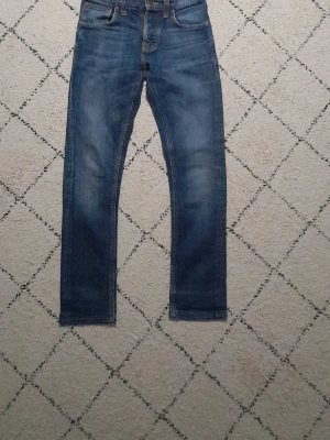 Nudie jeans Grim Tim  w27 L 32 - Snygga blå Nudie jeans med raka ben och diskreta slitningar framtill och baktill. Klassisk femficksmodell i denim med normalhög midja. Perfekta för en avslappnad och trendig look. Modellen är Grim Tim