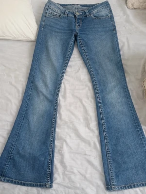 Blå bootcut jeans - Säljer ett par blå bootcut jeans med detaljerade bakfickor med knappar från gina 14+ . Jeansen har klassisk femficksmodell och normal midja. Perfekta för dig som gillar en retro och avslappnad stil. Super low waist