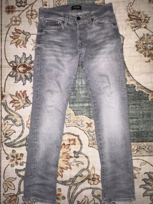 Ljusgrå slim fit jeans från jack and jones - Säljer ett par ljusgrå slim fit jeans med klassisk femficksdesign och normal midja. Jeansen har en något tvättad look och raka ben. Perfekta för dig som gillar en stilren och den trendiga stilen. Storlek 28/30-nypris 899