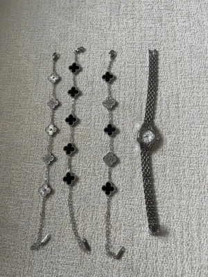Klocka+3 Silverfärgat armband med klövermotiv - Armband längd 18+5, klocka 19cm lätt att justera med en nål. Klockan är legering i bandet själva klockan är stål. 