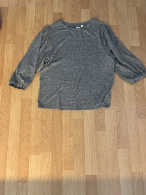 Grå långärmad topp från GAP - En enkel och stilren grå långärmad topp från GAP. Toppen har en rund halsringning och är tillverkad i mjukt material som känns skönt mot huden. Perfekt att matcha med jeans eller kjol för en avslappnad look.