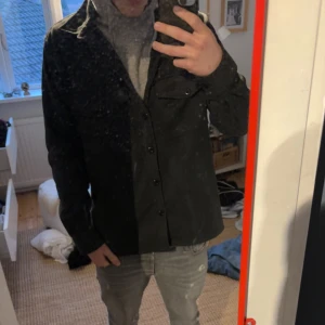 Svart overshirt med knappar - Snygg svart overshirt med knappar framtill. Perfekt för lager-på-lager-stil och passar bra till både jeans och chinos. Den har en klassisk krage och långa ärmar, vilket gör den idealisk för kyligare dagar.PRIS KAN DISKUTERAS 