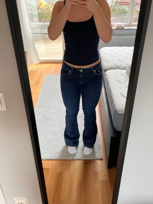 Mörkblå bootcut jeans från Lager 157 - Säljer ett par mörkblå bootcut jeans från Lager 157 med klassisk femficksdesign och låg midja. Jeansen har en snygg tvätt och subtila kontrastsömmar. Perfekta för dig som gillar en tidlös och avslappnad stil.