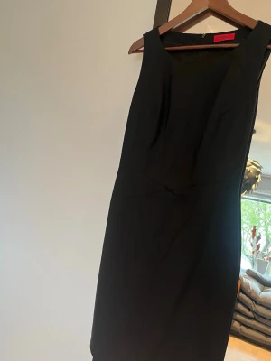 Ärmlös fodralklänning Hugo Boss - Klassisk svart ärmlös klänning från Hugo Boss med figurnära passform och rund halsringning. Perfekt för dig som gillar stilrena och tidlösa plagg. Enkel design utan mönster eller extra detaljer.