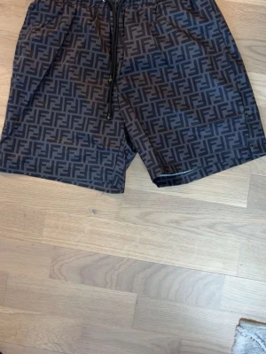Svarta Fendi shorts med FF-mönster - Snygga svarta shorts från Fendi med det klassiska FF-logomönstret över hela tyget. Shortsen har elastisk midja med snörning och är tillverkade i ett lätt och bekvämt material. Perfekta för en trendig och avslappnad stil.