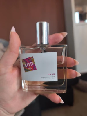 LQD LDN For Her Pheromone Parfum - En stilren parfym för henne från LQD LDN. Flaskan är fyrkantig i genomskinligt glas med en silverfärgad spraykork. Parfymen har en ljusgul ton och etiketten har färgglad design. Innehåller 50 ml pheromone parfum. Ca halva flaskan kvar