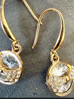 Guldiga örhängen med gnistrande stenar - Säljer ett par eleganta guldiga örhängen med rund form och gnistrande klara stenar. Örhängena har en krok för enkel användning och är dekorerade med små glittrande stenar som ger en lyxig känsla. Perfekta för att lyfta din stil med lite extra bling.stämpel äkta silver m.guldplätering.