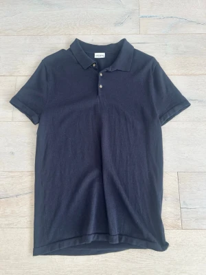 Mörkblå piké från John Henric - Klassisk mörkblå pikétröja från John Henric med krage och tre knappar framtill. T-shirten har korta ärmar och en stilren, tidlös design som passar till det mesta. Tillverkad i mjukt bomullsmaterial för en bekväm känsla.