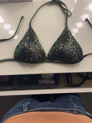 Grön paljettbikini med knyt - Jättesnygg bikinitopp i jättfint skick, som jag köpt av en tjej på vinted, tyckte inte riktigt att den passade mig därför säljer jag den vidare!! 