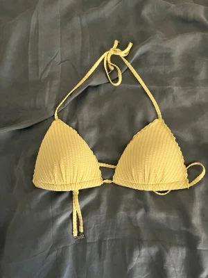 Gul ribbad trekantsbikini - Snygg gul trekantsbikini med ribbad struktur och knyt i nacken och ryggen. Små blommiga metalldetaljer på snörena framtill ger en extra touch. Perfekt för strandhäng och soliga dagar!