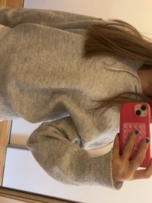 Ljusgrå stickad hoodie Gina Tricot - Mysig ljusgrå stickad hoodie från Gina Tricot med huva och långa ärmar. Tröjan har ribbstickade muddar vid ärmslut och nederkant, perfekt för en chill och avslappnad stil. Superenkel att matcha med jeans eller leggings.