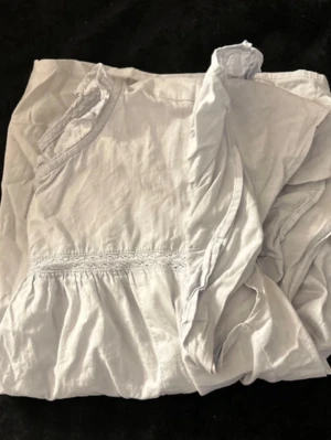 Vit blus med volangdetalj - Söt vit blus med korta ärmar och volangdetalj nedtill. Blusen har en lätt rynkad midja och små volanger vid ärmslut och halsringning. Tillverkad i ett tunt, mjukt tyg som känns luftigt och bekvämt.