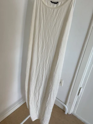 Vit långklänning i bomull - En enkel och stilren vit långklänning i mjuk bomull. Klänningen är ärmlös med rund halsringning och har en rak, avslappnad passform. Perfekt för varma dagar och enkel att styla med accessoarer.
