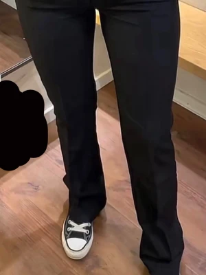Svarta kostymbyxor med utsvängda ben - Snygga svarta kostymbyxor med utsvängda ben och pressveck. Byxorna har hällor för skärp och sidfickor. Perfekta för en stilren look och passar till sneakers eller boots. Materialet ser ut att vara en mjuk och följsam väv.